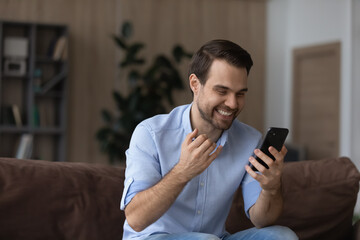 Overjoyed young man looking at telephone screen, celebrating getting amazing news, reading message with online lottery gambling auction win, feeling excited at home, internet success concept.