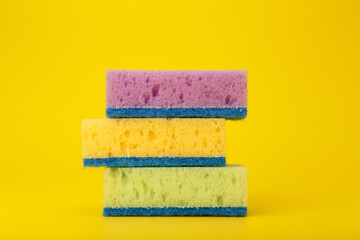 Close up of stack of three multicolored cleaning or kitchen sponges on bright yellow background