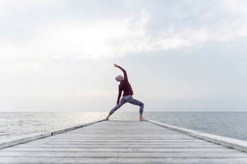 Woman practicing Utthita Parsvakonasana pose on pier