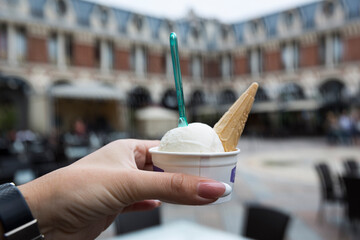 A beautiful female hand holds a cardboard glass with ice cream. Cocktail, juice, lemonade. But the backdrop of the old city.