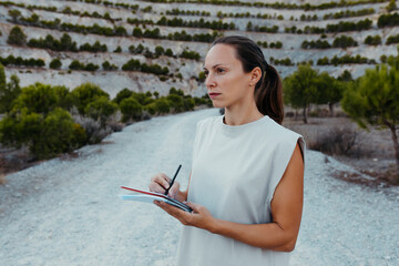 Female scientist collecting data in book while doing research in old mine