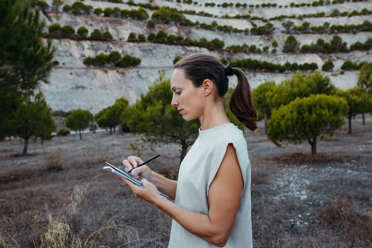 Female scientist writing data in book while doing research in field