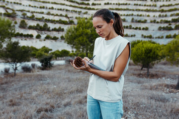 Female expertise collecting data of pine cones in book at old mine
