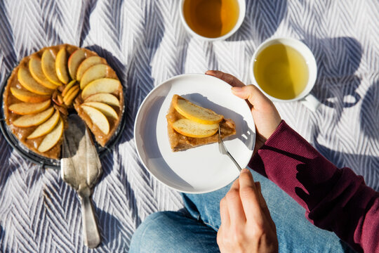 Hands of young woman eating freshly baked apple pie on picnic blanket