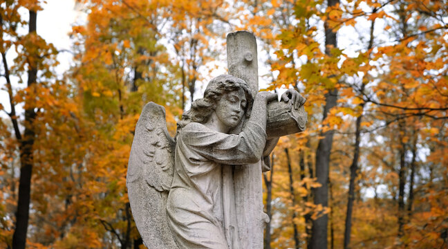 angel statue and cross on old cemetery, autumn natural background. concept of religion, faith, Remember, mourn, memory. all saints day, All Souls Day. Design for condolences, mourning cards