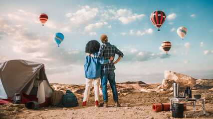 Young Diverse Tourist Couple Hiking and Living in a Tent in Great Outdoors in Rocky Canyon Valley. Male and Female Backpacker Hug and Look at Hot Air Balloon Festival in Mountain National Park.