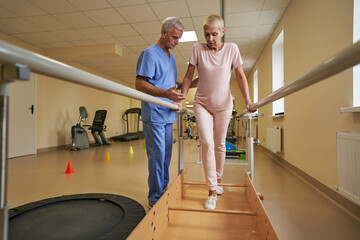 Female patient walking between parallel bars at rehabilitation room