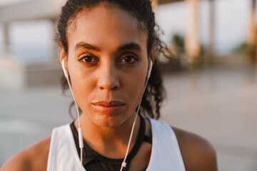 Black sportswoman listening music while working out on parking