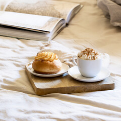 Cup of  coffee with whipped cream and sweet bun o the wooden try in the bed sheets. Slow food concept.