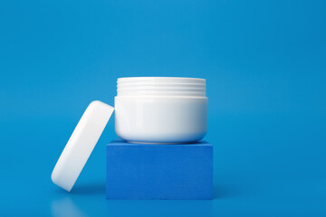 Opened cosmetic jar on dark blue pedestal on blue background. Concept of repairing nourishing night cream or lotion