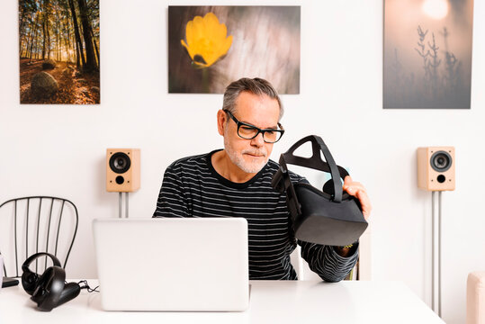Mature man with laptop examining virtual reality simulator at home