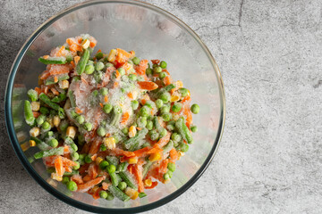 Frozen mixed vegetables, including carrots, beans, peas and sweet corn, defrosting in a glass bowl.  On a concrete background