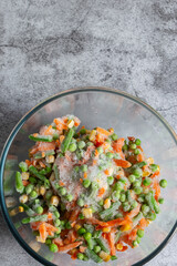 Frozen mixed vegetables, including carrots, beans, peas and sweet corn, defrosting in a glass bowl.  On a concrete background