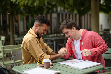 Young man with Down syndrome with his mentoring friend arm wrestling outdoors in cafe