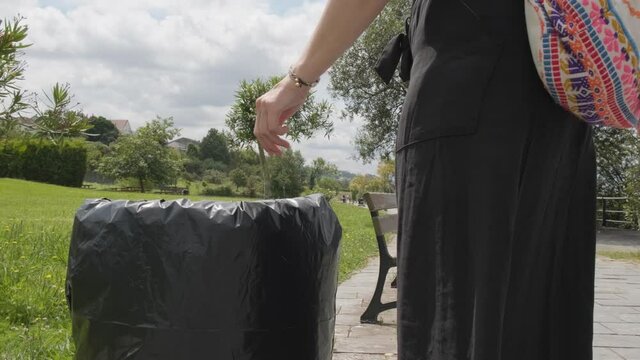Woman environmentalist throwing empty water bottle into trash can in the park