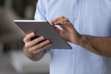 Close up young man using digital computer tablet applications, web surfing information online, choosing goods shopping in internet store, communicating in social networks, spending time online.