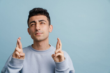 Young middle eastern man holding fingers crossed for good luck