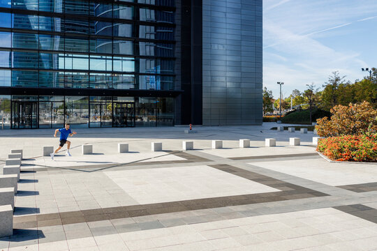 Young male athlete running on footpath in front of building