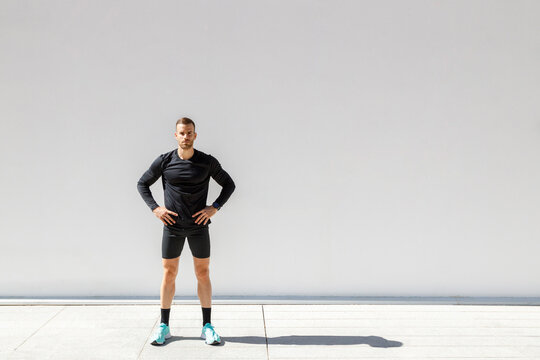 Young sportsman standing with hands on hips in front of white wall