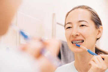 Young woman with braces cleans her teeth with a special dental brush, before mirror. Dental and...