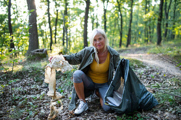 Senior woman ecologist picking up waste outdoors in forest.
