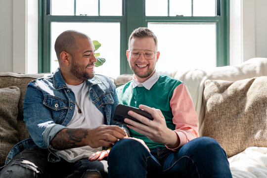 Gay couple taking selfies, sitting on a couch at home