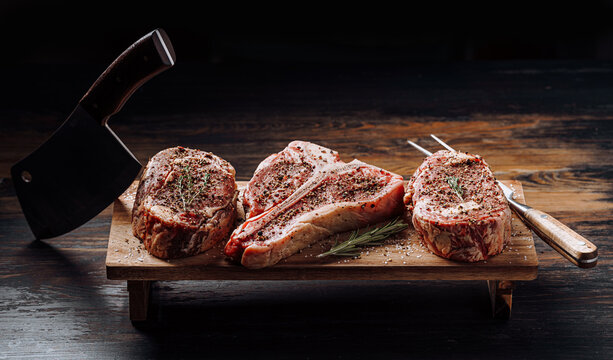 three lovely raw marbled black Angus beef steaks flavored with a mixture of ground pepper and ready to cook and serve on a dark wooden background.