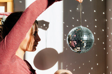 Young lonely woman holding shiny disco ball at home