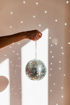 Young woman holding shiny disco ball in front of wall at home