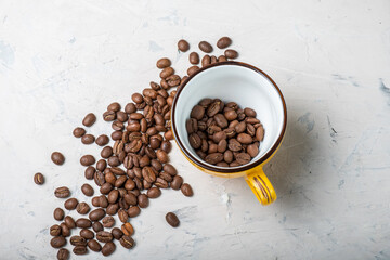 Grains of coffee and a yellow mug on a textured beige background, top view.