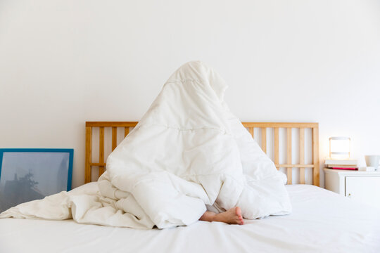 Young woman wrapped in white blanket while sitting on bed at home