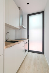 A small new kitchen with oven, stove and extractor. Interior with white cabinets and wooden counter top.
