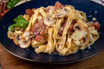 Tagliatelle in a creamy sauce with mushrooms and parmesan close-up in a blue plate.
