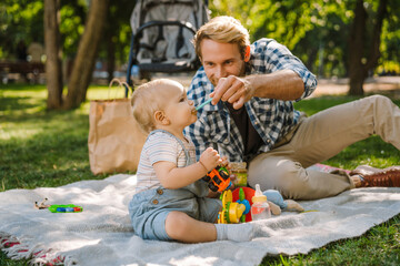 White father feeding his son while resting on blanket at park