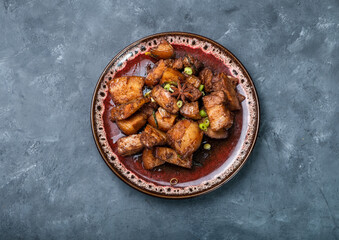 Traditional Chinese braised pork belly on a dark textured background. One plate with a dish. Top view, free space.