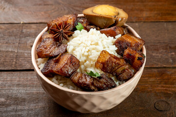 Bowl with rice and stewed pork belly close-up on a wooden background.