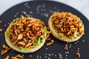 vegan shredded marinated teriyaki tofu with avocado guacamole on top of English muffins, healthy plant-based food