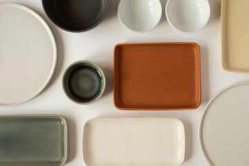 Neutral colour handmade ceramics, empty craft ceramic plates and bowls on white background. Flat lay, top view