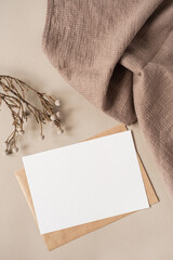 Blank paper sheet card with mockup copy space and dry floral branch and blanket cloth on neutral beige background. Minimal aesthetic business brand template. Flat lay, top view