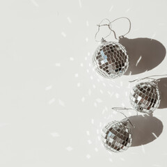 Small mirror disco balls with sunlight shadows on white background. Minimal aesthetic holiday celebration party concept