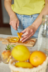Obraz na płótnie Canvas Female hand cut orange, Woman preparing, making citrus and rosemary fresh lemonade in glass on a white table at home, summer drink, detox healthy water.