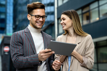 Businessman and businesswoman discussing working together in urban background outdoors.