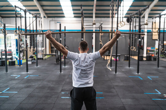 Young male athlete stretching arms with stick in gym