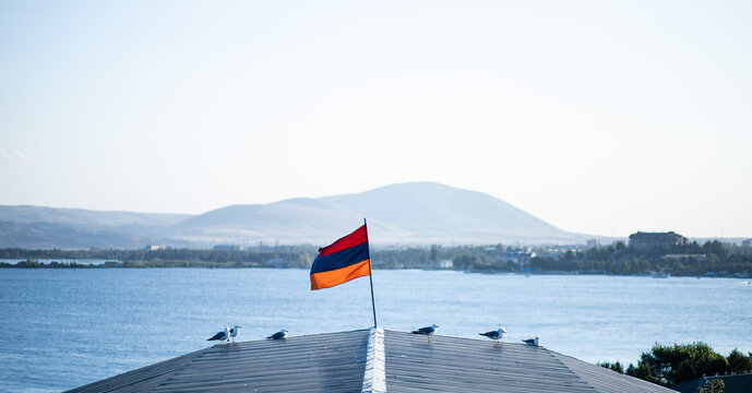 Group of gulls perched on a roof with an Armenian flag on the bay of Lake Sevan in Armenia