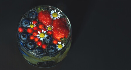 A glass with a fragrant drink made of fresh berries and chamomile, top view. Layout with space for text, on a dark background. Flat lay, copy space.
