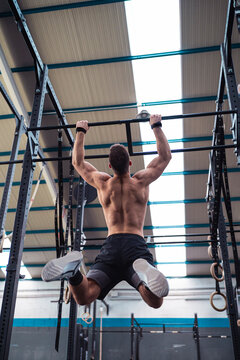 Shirtless male athlete hanging on monkey bars while exercising in gym
