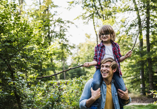 Happy father carrying son on shoulders in forest