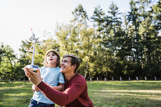 Father holding wind turbine model with son at park