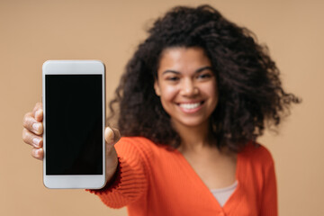 Smiling curly haired African American woman showing mobile phone screen isolated on background,...
