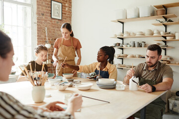 Warm toned portrait of diverse group of people decorating ceramics in pottery workshop, copy space